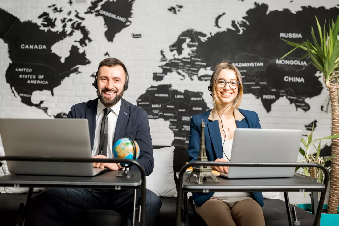 couple-travel-managers-working-online-with-laptops-headsets-agency-office-with-world-map-background
